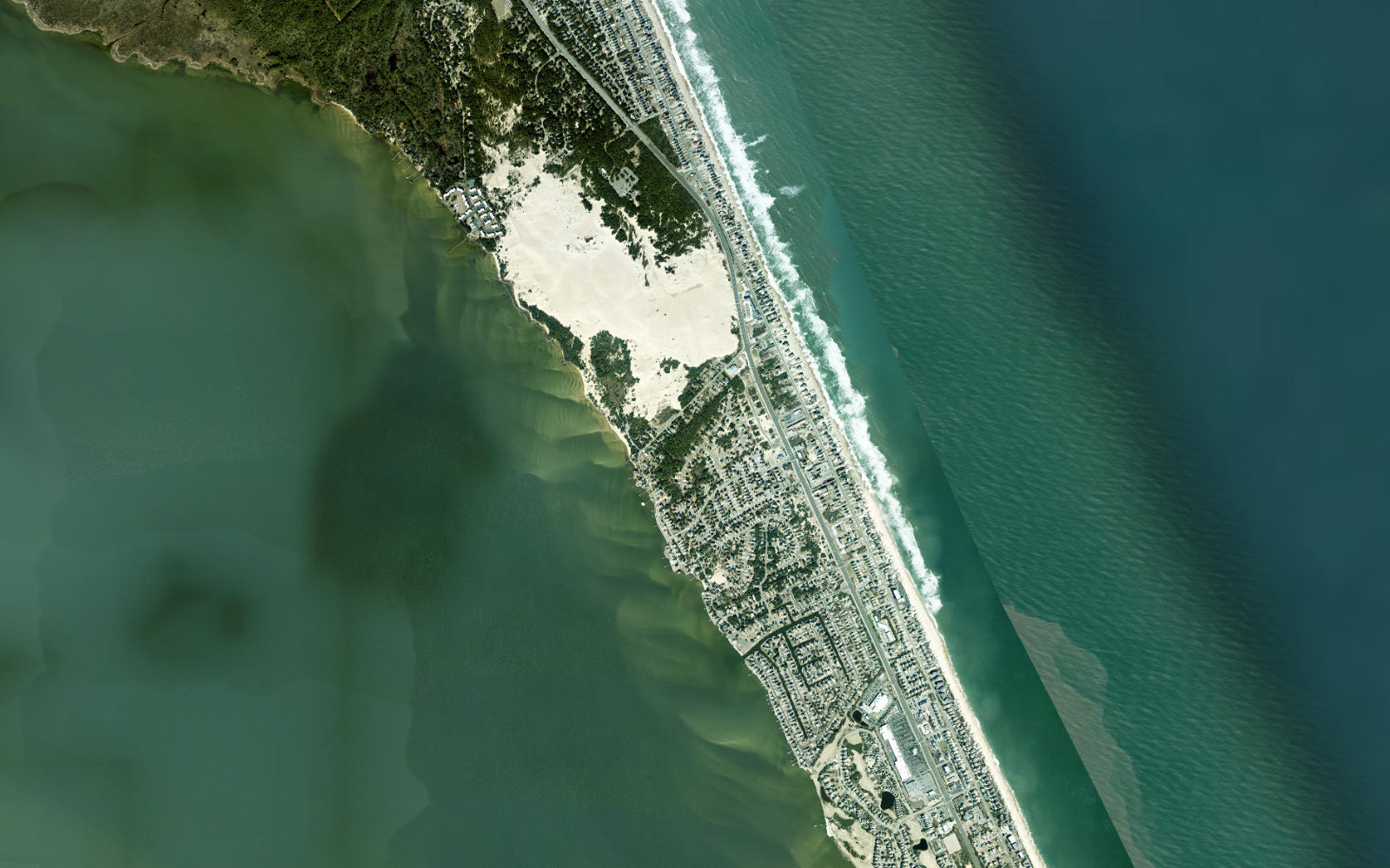 A wide aerial of the Nags Head barrier island on the Outer Banks: the Atlantic to the east, Roanoke Sound to the west, and the developed strip between them