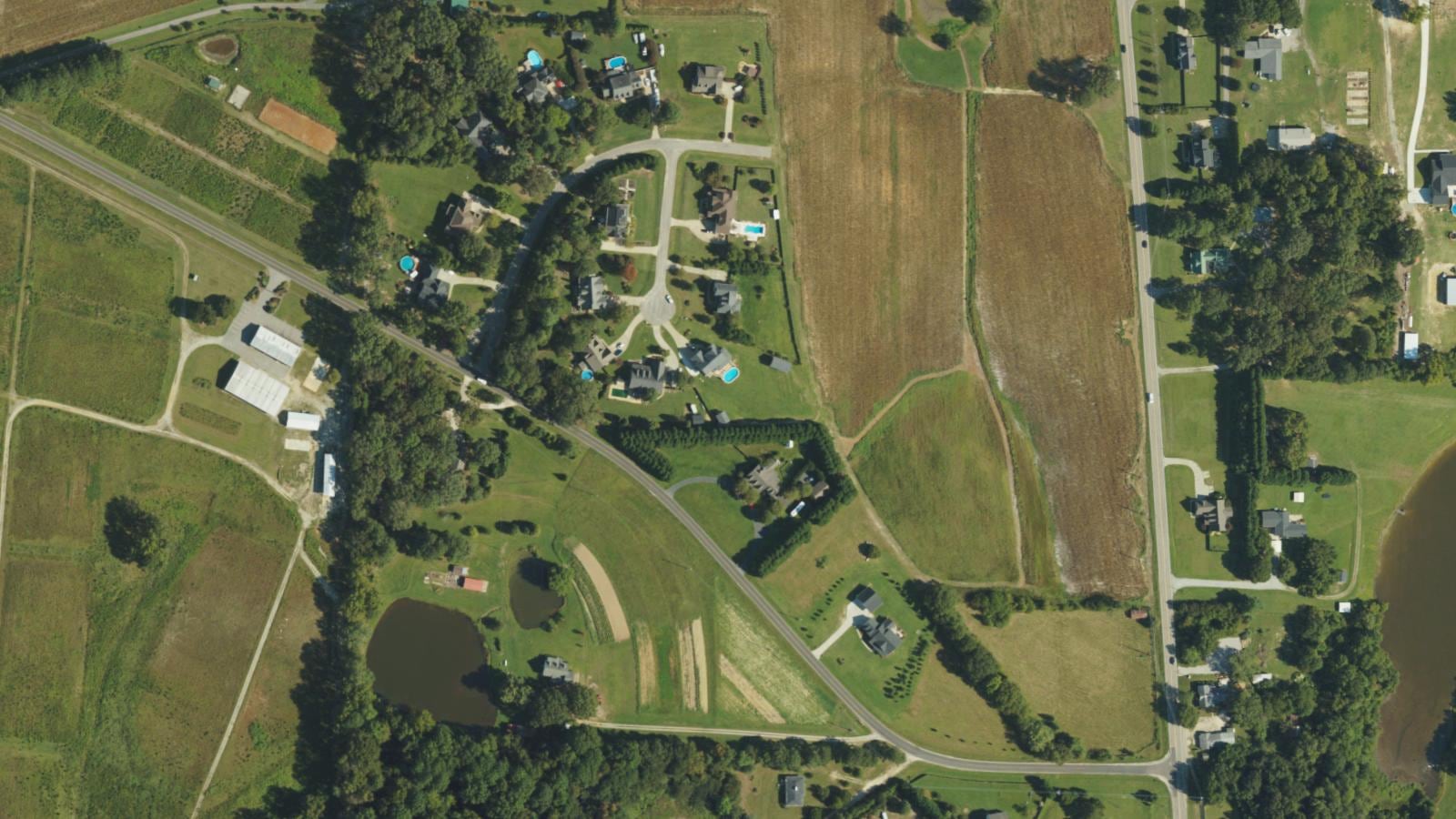 Summer aerial of an open crop field on Piney Grove Wilbon Road near Holly Springs, North Carolina, beside a neighborhood of large-lot homes.
